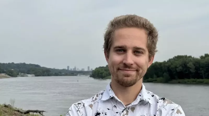 Adam Dullinger poses in front of a body of water